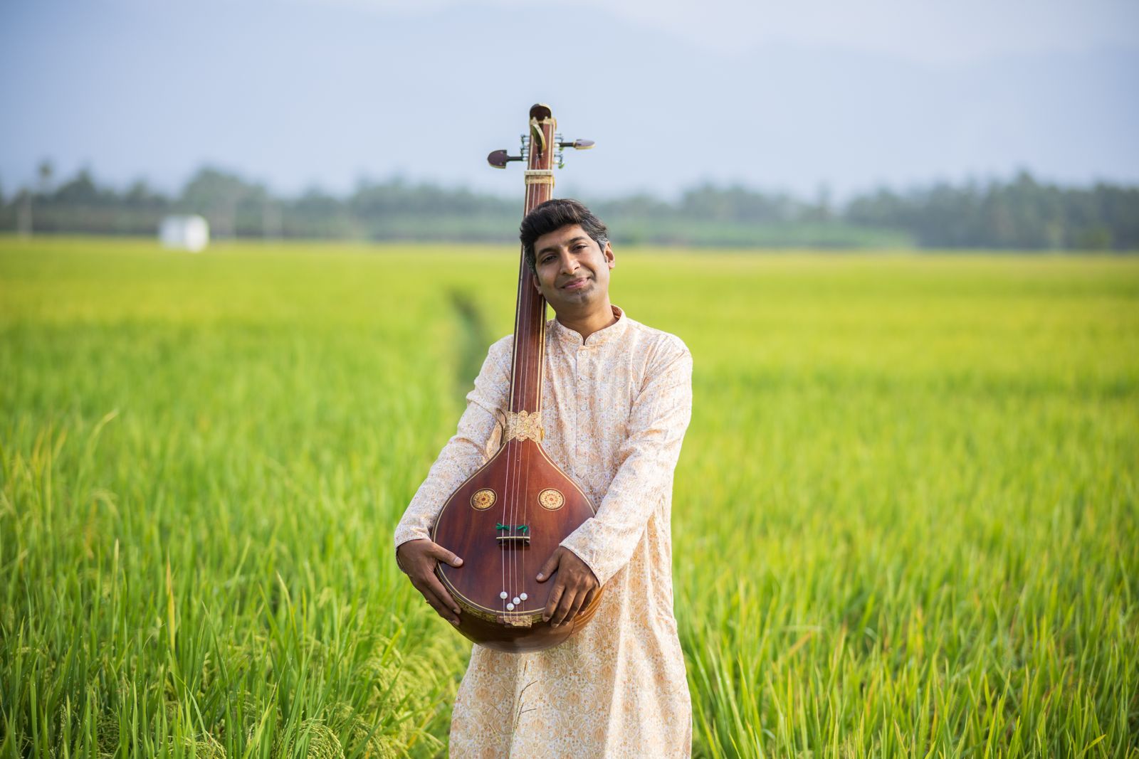 Dr. Koustubh Pare holding a tanpura in a lush green field