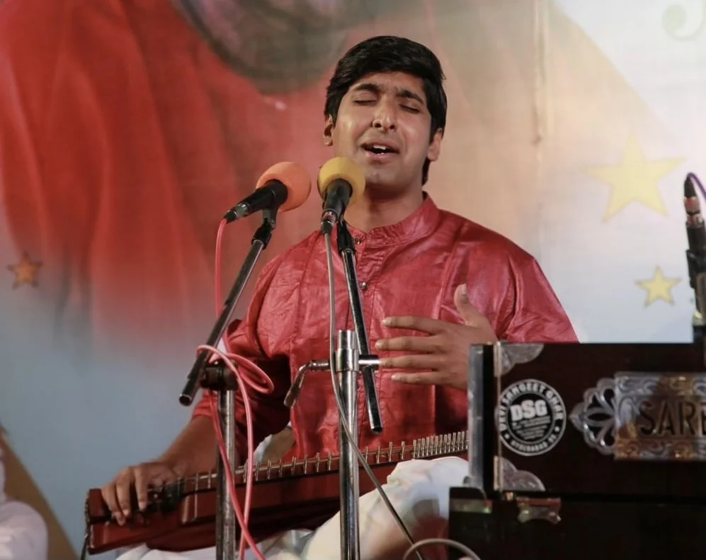 Dr. Koustubh Pare performing with swarmandal before a spiritual stage backdrop
